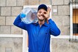 Young hispanic man holding a gallon bottle of water for delivery smiling happy doing ok sign with hand on eye looking through fingers