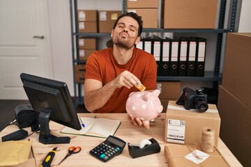 Poster - Young hispanic man working at small business ecommerce holding piggy bank looking at the camera blowing a kiss being lovely and sexy. love expression.