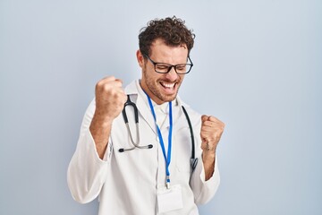 Sticker - Young hispanic man wearing doctor uniform and stethoscope very happy and excited doing winner gesture with arms raised, smiling and screaming for success. celebration concept.