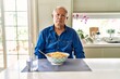 Senior man with grey hair eating pasta spaghetti at home relaxed with serious expression on face. simple and natural looking at the camera.