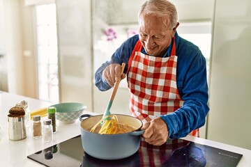 Senior man smiling confident cooking spaghetti at kitchen