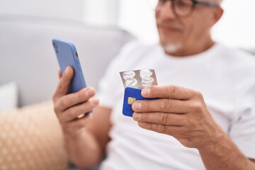 Sticker - Middle age grey-haired man using smartphone and credit card holding pills at home