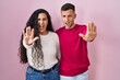 © Krakenimages.com - Young hispanic couple standing over pink background doing stop gesture with hands palms, angry and frustration expression