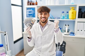 Sticker - Arab man with beard working at scientist laboratory holding money screaming proud, celebrating victory and success very excited with raised arms