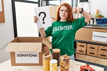 Sticker - Young redhead woman wearing volunteer t shirt holding question mark with angry face, negative sign showing dislike with thumbs down, rejection concept