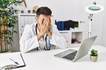 Poster - Young doctor working at the clinic using computer laptop with sad expression covering face with hands while crying. depression concept.