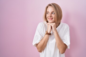 Poster - Young caucasian woman standing over pink background laughing nervous and excited with hands on chin looking to the side