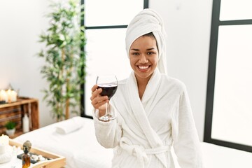 Poster - Young latin woman wearing bathrobe toasting with wine at beauty center