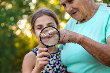 Canvas Print - Grandmother and child are studying the snail in the park. Selective focus.