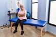 © Krakenimages.com - Senior grey-haired woman physitherapist patient sitting on massage table with arms crossed gesture at physitherapy clinic