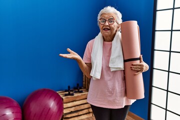 Wall Mural - Senior woman with grey hair holding yoga mat celebrating achievement with happy smile and winner expression with raised hand