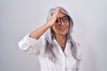 Wall Mural - Middle age woman with tattoos wearing glasses standing over white background doing ok gesture with hand smiling, eye looking through fingers with happy face.