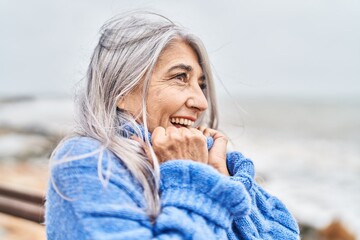 Middle age grey-haired woman smiling confident looking to the side at seaside