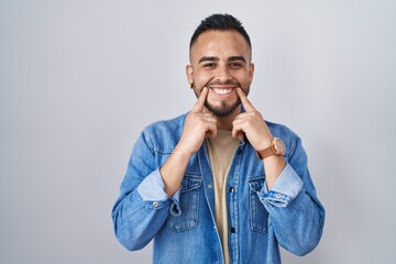 Poster - Young hispanic man standing over isolated background smiling with open mouth, fingers pointing and forcing cheerful smile