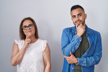 Poster - Hispanic mother and son standing together with hand on chin thinking about question, pensive expression. smiling and thoughtful face. doubt concept.