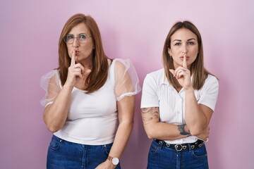 Sticker - Hispanic mother and daughter wearing casual white t shirt over pink background asking to be quiet with finger on lips. silence and secret concept.