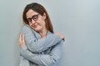 © Krakenimages.com - Brunette woman standing over grey background hugging oneself happy and positive, smiling confident. self love and self care
