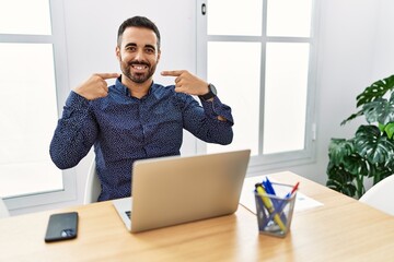 Sticker - Young hispanic man with beard working at the office with laptop smiling cheerful showing and pointing with fingers teeth and mouth. dental health concept.