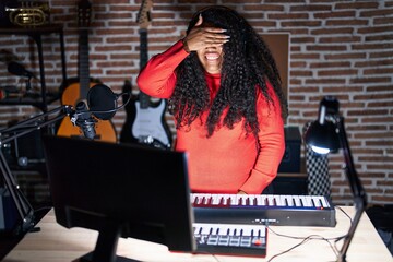 Poster - Plus size hispanic woman playing piano at music studio smiling and laughing with hand on face covering eyes for surprise. blind concept.