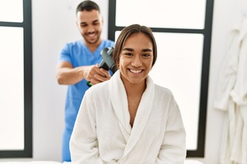 Sticker - Latin man and woman wearing physiotherapy uniform massaging neck using percussion gun at beauty center