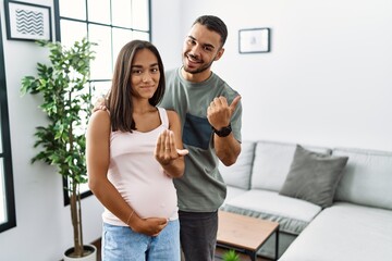 Canvas Print - Young interracial couple expecting a baby, touching pregnant belly beckoning come here gesture with hand inviting welcoming happy and smiling