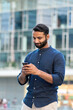 © insta_photos - Indian business man, eastern businessman holding cellphone using mobile phone banking app, making e payment, texting message, reading news standing in urban city on modern street outdoors, vertical.