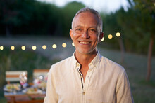 Portrait Of Happy Mature Man Looking At Camera Outdoor. Senior People With White Hair Feeling Confident At Sunset. Closeup Face Of Smiling With Backyard In Background.