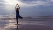 © bunditinay - Asian woman warm up and play yoga exercise on the beach by the sea at morning sky background.