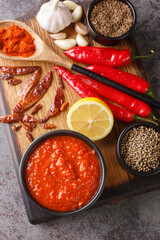 Wall Mural - Harissa Paste North African spicy red sauce to add heat to dressings, sauces, soups in bowl on wooden board with ingredients closeup. Vertical top view from above