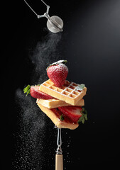 Waffles with strawberries sprinkled with sugar powder.