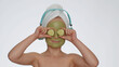 © Andrii Iemelianenko - Smiling young child girl after bath in towel on head and moisturizing green cucumber facial mask listening to music on headphones, dancing. Female teenager kid skin care treatment, natural cosmetics