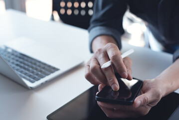 Poster - Close up of business man hand holding and using mobile smart phone with stylus pen, digital tablet and laptop computer on office table, surfing the internet