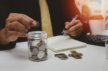 Wall Mural - Man hand putting money coin and take note of income and expenses and working to save money for the future growing business, education and retirement.