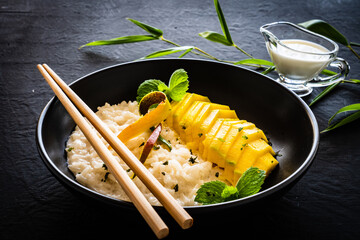 Rice in coconut milk with mango and mint on black wooden table