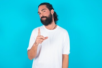 young bearded man wearing white T-shirt over blue studio background frustrated and pointing to the front