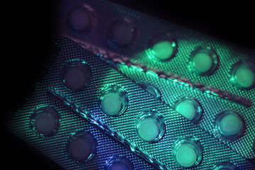Fototapete - Pills or drugs in a package under neon light on a dark background pattern for design..
