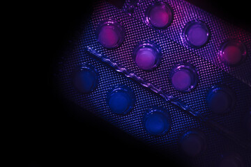 Fototapete - Pills or drugs in a package under neon light on a dark background pattern for design..