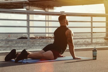 Muscular bearded man sportsman with cap doing sport exercising outdoors in urban embankment. Fitness healthy lifestyle concept with male athlete, exercising in city outside. Copy text space