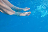 Fototapeta Łazienka - Women's legs in the pool water. Barefoot and blue swimming pool wavy water background, great for your background and space for text