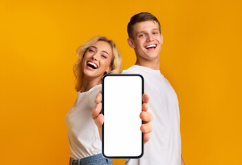 Laughing happy young caucasian male and female with open mouth show smartphone with empty screen