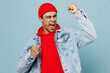 Young middle eastern man 20s he wear denim jacket red hat doing winner gesture celebrate clenching fists say yes isolated on plain pastel light blue cyan background studio. People lifestyle concept.
