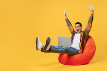 Full Body Young Middle Eastern Man Wear Casual Shirt White T-shirt Sit In Bag Chair IT Woman Hold Use Work On Laptop Pc Computer Raise Up Hands Finish Job Isolated On Plain Yellow Background Studio