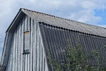 Sticker - wooden attic of a rural house with a small window under a gray slate roof on the street against the sky