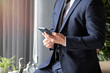 © Наталья Жукова - young businessman in a dark blue suit working in the office, typing on a mobile phone