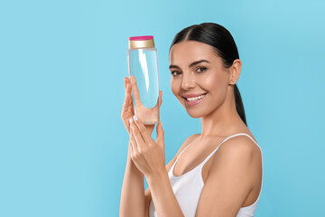 Young woman with bottle of micellar water on light blue background