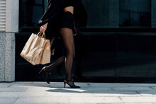 Close-up Side View Of A Woman In High Heel Stilettos Walking Down The Street Carrying A Shopping Bag