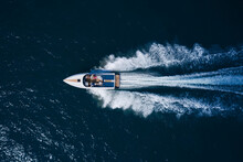 A White Large Open Boat With People Is Moving Quickly On Dark Water. Top View. White Speedboat Fast Movement On Dark Water Top View.