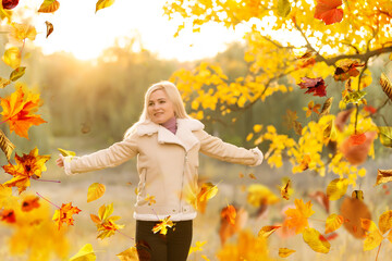 Wall Mural - Beautiful girl walking outdoors in autumn. Smiling girl collects yellow leaves in autumn. Young woman enjoying autumn weather.