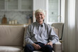 © fizkes - Happy senior elder 60s man indoor home portrait. Positive retired businessman, homeowner in casual looking at camera with toothy smile, laughing, making video call from sofa. Retirement