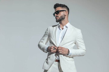 bearded businessman with sunglasses buttoning white suit